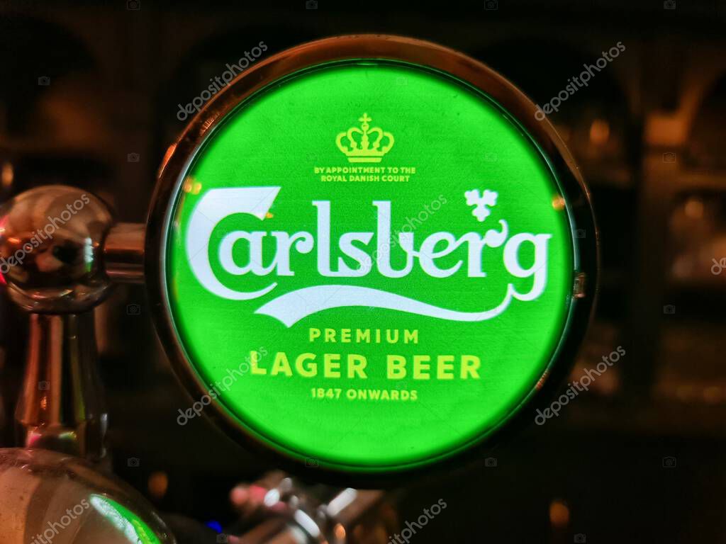 Kiel, Germany - 05. November 2025: Carlsberg beer tap sign, illuminated with green light, in a pub environment
