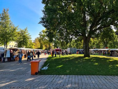 Neumuenster, Almanya - 28. Eylül 2025: İnsanlar güneşli bir günün tadını çıkarıyor, bir kasaba parkındaki canlı bir açık hava pazarında çeşitli tezgah ve ürünlere göz atıyorlar