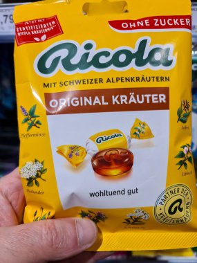 Kiel, Almanya - 24. Kasım 2025: El ele tutuşan sarı Ricola Orijinal Kruter şekersiz öksürük pastilleri ve boğaz rahatlatıcı doğal alp bitkileri 