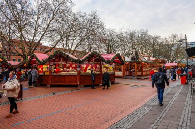 Kiel, Almanya - 01. Aralık 2025: Geleneksel ahşap tezgahların arasında yürüyen, neşeli çelenklerle süslenmiş insanlar, Avrupa 'daki bir Noel pazarında çeşitli ürünler satıyorlar