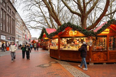 Kiel, Almanya - 01. Aralık 2025: İnsanlar, kentsel bir sokakta ışık ve çelenklerle süslenmiş Noel pazarlarında alışveriş yapıyor, kış tatillerinin keyfini çıkarıyorlar