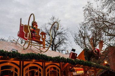 Kiel, Almanya - 01. Aralık 2025: Noel pazarında Noel Baba şapkası takan bir geyik kafası ve kızakla sallanan bir elf ziyaretçi çekiyor