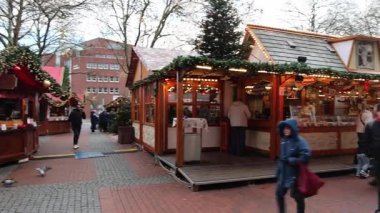 Kiel, Almanya - 02. Aralık 2025: Kiel Noel pazarındaki şenlikli atmosferde insanlar yanan ahşap tezgahların ve geleneksel bir atlıkarınca dönüşünün yanından geçiyorlar