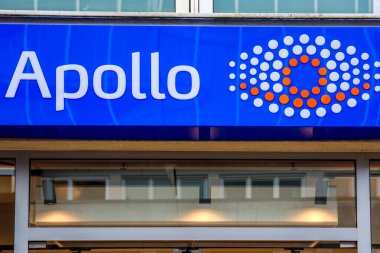 Kiel, Almanya - 01. Aralık 2025: Almanya 'nın Kiel kentindeki inşaat cephesinde belirgin nokta desenli logo içeren APOLO-Optik mağaza tabelası, mavi-beyaz-turuncu marka, kentsel sahne