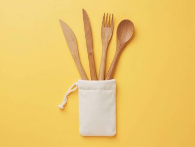 Çatal, kaşık ve bıçaklardan oluşan ahşap çatal takımı sarı arka plandaki pamuk torbadan çıkıyor.