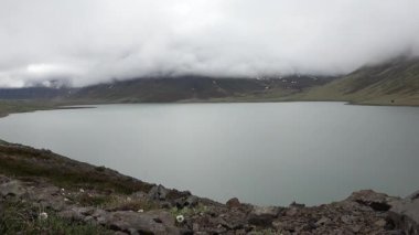 İzlanda 'nın dağlık kesimlerinde bulutlar bulutlu bir günde sakin bir dağ gölünün üzerinde hareket ediyor.