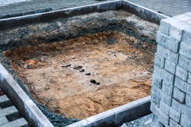 İnşaat için zemin kazılmış bir çukur ve istiflenmiş kaldırım taşlarını gösteriyor.