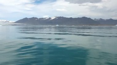 Buzdağları ve buzdağları olan bir buzul gölünün sakin sularında yelken açan bakış açısı