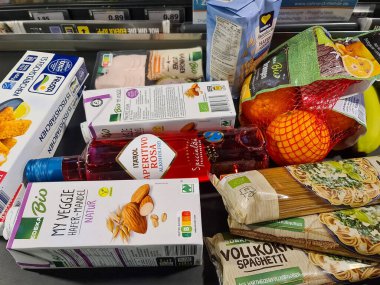 Kiel, Almanya - 07. Ocak 2026: Bir Alman süpermarket kasiyerinde nakliye bandında bekleyen çeşitli paketlenmiş ve taze gıda ürünleri