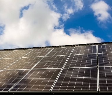 Güneşli gökyüzünün altında yenilenebilir elektrik üreten bir çatıyı kaplayan güneş panelleri