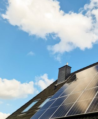 Bir evin çatısındaki güneş panelleri mavi gökyüzünün altındaki güneş enerjisini yakalıyor.