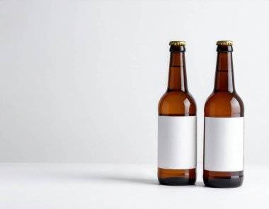 Beyaz bir yüzeyde duran boş beyaz etiketli iki kehribar rengi cam şişe, ürün modeli konsepti.