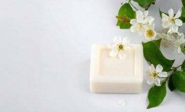 Narin beyaz çiçekli beyaz sabun ve temiz arka planda yeşil yapraklar doğal güzelliği ve organik hijyeni sembolize ediyor.