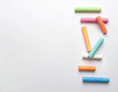 Yaratıcılığı ve eğitimi sembolize eden, temiz beyaz bir arkaplan üzerine yerleştirilmiş çeşitli renkli pastel tebeşir çubukları.