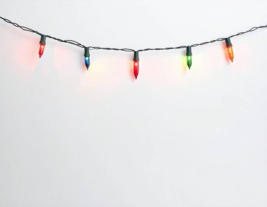 Noel sicim ışıkları basit beyaz bir arkaplanı aydınlatıyor, neşeli ve parıltılı bir tatil süsü yaratıyor.