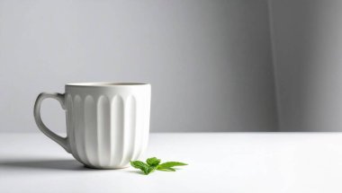 Beyaz seramik kupa flüt tasarımı ile sıcak bir içecek, temiz bir yüzey üzerinde canlı yeşil nane yaprakları eşliğinde
