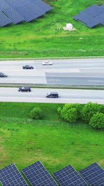 Yakınlardaki bir otoyolda fotovoltaik panelleri ve arabaları olan bir güneş çiftliğinin hava görüntüsü.
