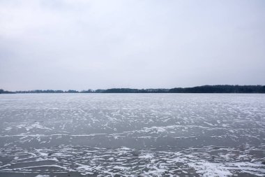 Soğuk bir kış günü, bulutlu bir gökyüzünün altında soyut buz kalıplarıyla donmuş göl yüzeyi.
