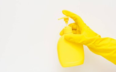 Beyaz arka planda sarı lastik eldiven takan, elinde sıvı sabun olan sarı bir şişe var. Konsept - hijyen, temizlik