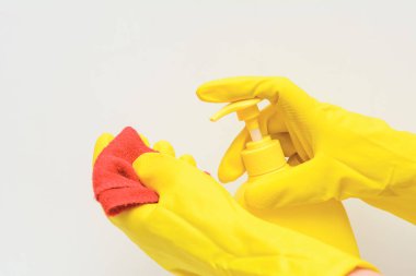 Beyaz arka planda sarı lastik eldiven takan, elinde sıvı sabun olan sarı bir şişe var. Diğer elinde ise kırmızı bir bez parçası var. Konsept - hijyen, temizlik
