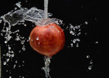 Siyah arka planda, bir nar meyvesi bir su jetinin üzerine düşer. Siyah arka plana düşer. Kavram-meyve diyeti, vitaminler