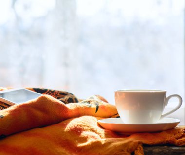 Yatak örtüsünün üzerinde bir akıllı telefon var. Yanında da bir fincan kahve var. Arka planda bahar ışığı olan bir pencere var. Kavram- uzak çalışma