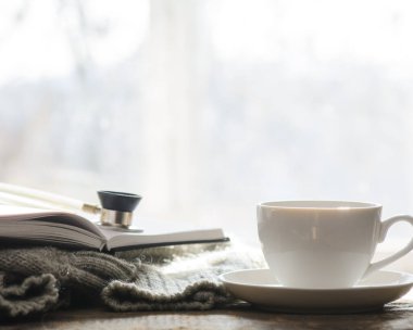 Kazağın üzerinde bir günlük var. Günlükte steteskop var. Yanında da bir fincan kahve var. Arka planda bahar ışığı olan bir pencere var. Baskıyı gözlemle