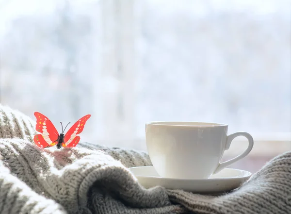 A butterfly sits on the sweater. There\'s a cup of coffee next to it. Against the background of a spring window. Concept-breakfast, business.