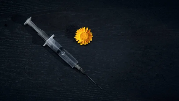 On a black background - a syringe with a vaccine. Next to it is a yellow flower-a symbol of life. . A concept vaccine as a salvation from infection