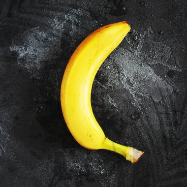 Kalıplı siyah bir zeminde taze sarı muz, su damlaları ve palmiye yapraklarının gölgesi. Enerji veren ve sağlıklı olan tropik doğal organik meyveler. Afrika ve Asya ülkelerinin ürünleri