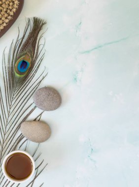 Tavus kuşu tüyü, masaj taşları, yağ ve vücut fırçasıyla bezenmiş düz bir bileşim açık mavi mermer arka planda. Cilt bakımı ve kaplıca rahatlama konsepti. Sağlık kaplıcası arka planı, dikey bileşim