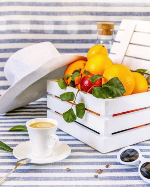 Yaz, bir fincan kahveyle sabah natürmortu. Tekstil arka planında tahta bir kutuda olgun portakallar. Sağlıklı, mevsimlik yiyecekler. Çiftlik, yerel meyveler. Hasat Günü Kutlaması. Akdeniz yemekleri