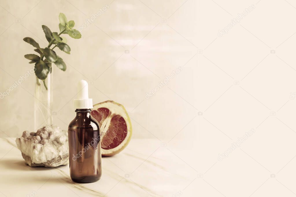 Citrus essential oil, grapefruit, stone and green kalanchoe branch on marble background with copy space. Alternative medicine and natural skin care. Home made product for beauty care. Glow serum