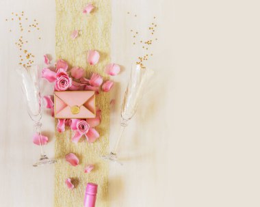 İki bardakla romantik şenlikli bir hayat, bir şişe gül şarabı, bir hediye kutusu ve beyaz arka planda kopyalanmış gül yaprakları. Sevgililer Günü. Büyük bir aşkla geçen küçük anlar. aşk bayramı kartı