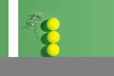 Tenis mi? Üç sarı tenis topu ve çiçekli bahar sporu kompozisyonu sert tenis kortunun yeşil arka planında fotokopi alanı ile. Açık hava sporları konsepti. Düz yatıyordu