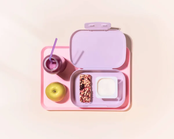 Boîte à lunch avec yaourt, bar à céréales, pomme et cocktail de baies d'avoine sur fond rose — Photo