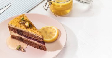 Dikey yemek kompozisyonu, bir parça şam fıstıklı limonlu turta pembe bir tabakta bal ve fındıklı fındık ve beyaz arka planda bir kavanoz bal ile fotokopi alanı. Sağlıklı tatlı hamur işleri