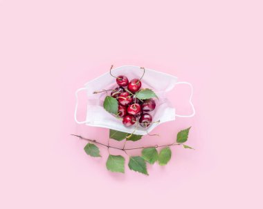 Sağlık hizmetleri yaz kompozisyonu, pembe arka planda kirazlı ilaç maskesi. Virüslerden korunmak için bol vitamin ve besin içeren sağlıklı mevsimsel meyve ve sebze kavramı