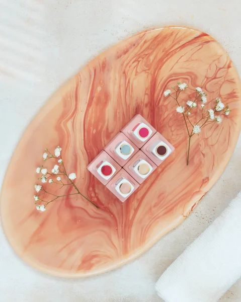 Jars of nail polish on a smalt pink stand and a white rolled-up towel on a textured, light table — Stock Photo, Image