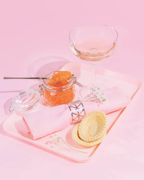 Vertical, pink, food composition with a jar of salmon red caviar, tartlets and a glass of rose wine — Stock Photo, Image