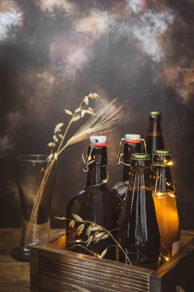 Flessen met koud, licht en donker, ongefilterd bier met tarweoren in het lege glas op een meegebrachte achtergrond — Stockfoto