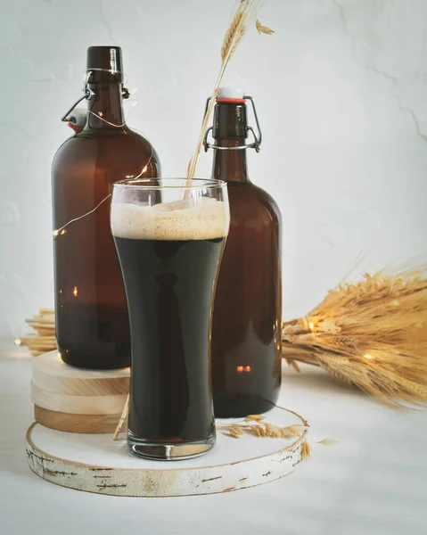 Glas donker ongefilterd bier, twee donkerbruine flessen en een boeket tarwe op een witte achtergrond — Stockfoto