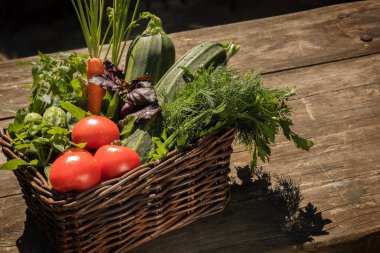 Yerel yetiştirilmiş, sepetteki sebzeler ahşap kahverengi bir masada.