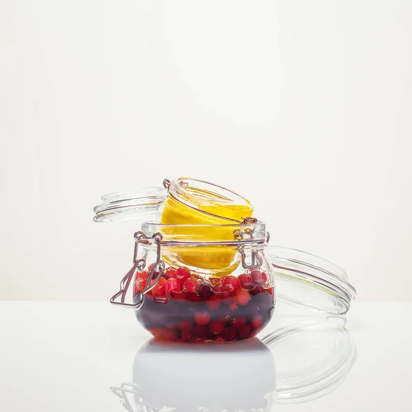 Szklane słoiki ze sfermentowaną żurawiną miodową i cytryną na białym tle — Zdjęcie stockowe