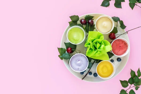 Yazlık yemek kompozisyonu çeşitli ev yapımı, vegan, meyve dondurması, yapraklar, yabanmersini ve kirazlar pembe arka planda yazılı. Sütsüz, meyveli dondurma veya donmuş yoğurt.