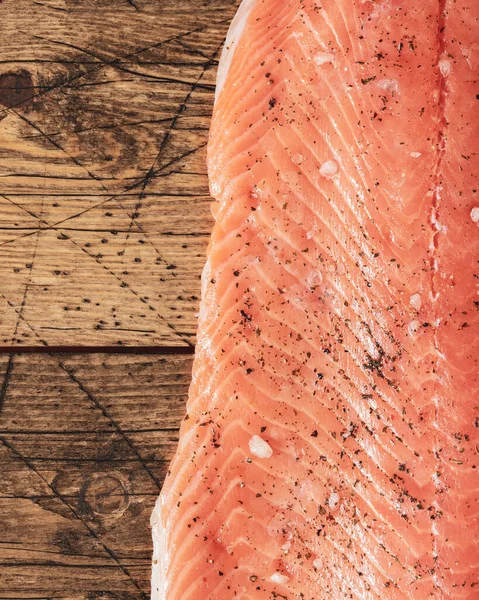 Raw salmon fillet with spices and salt on a wooden background