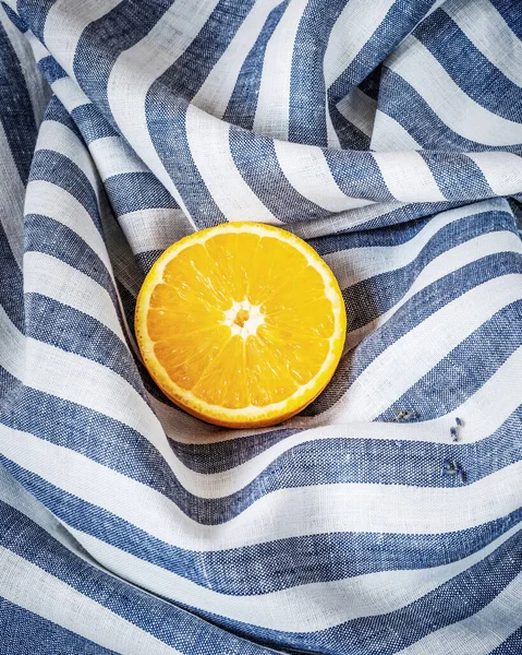 Το μισό φρέσκο, ώριμο πορτοκάλι σε ριγέ υφασμάτινο φόντο — Φωτογραφία Αρχείου