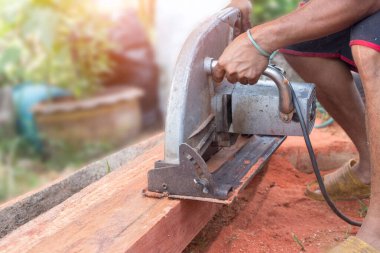 Yeni bir ev yapım projesinin tahtalarını kesmek için el yapımı solucan sürücüsü kullanan bir inşaat işçisi. Tahta keserken dairesel bir testere.