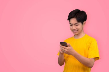 Mutlu gülümseyen Asyalı genç adam cep telefonunu renkli pembe arka planda açık bir şekilde gösteriyor.