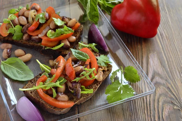 Rye bruschetta with beans, sweet peppers, arugula and red onion — Stock Photo, Image
